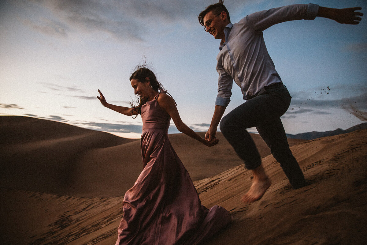 man and woman wearing pink dress runs down great sand dunes national park