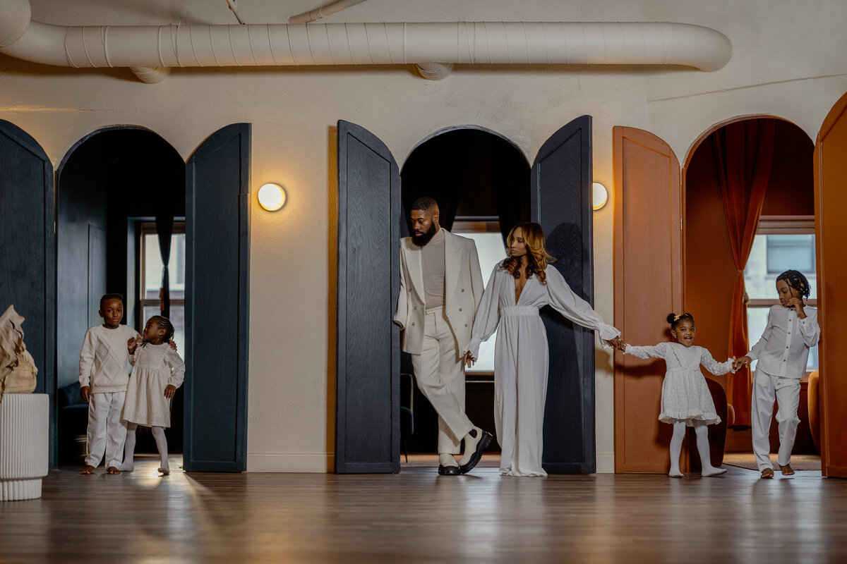 Black family of six posing elegantly for a magazine-style photoshoot with a Fort Worth, Texas photographer. The family is dressed in coordinated, stylish attire, showcasing their unity and grace against a modern backdrop with colorful arches, creating a stylish and luxury family portrait.