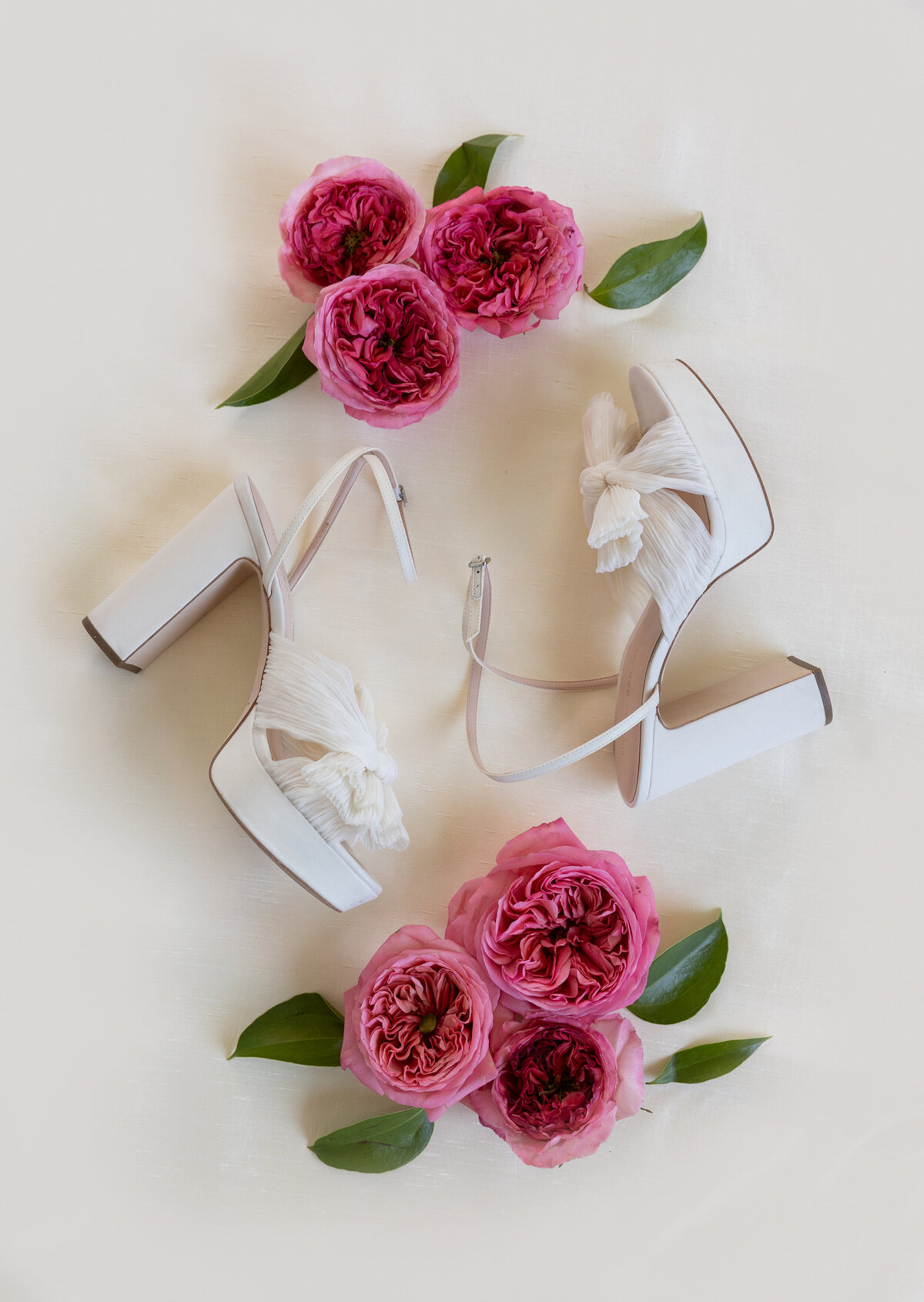 A pair of white bridal shoes and pink flowers