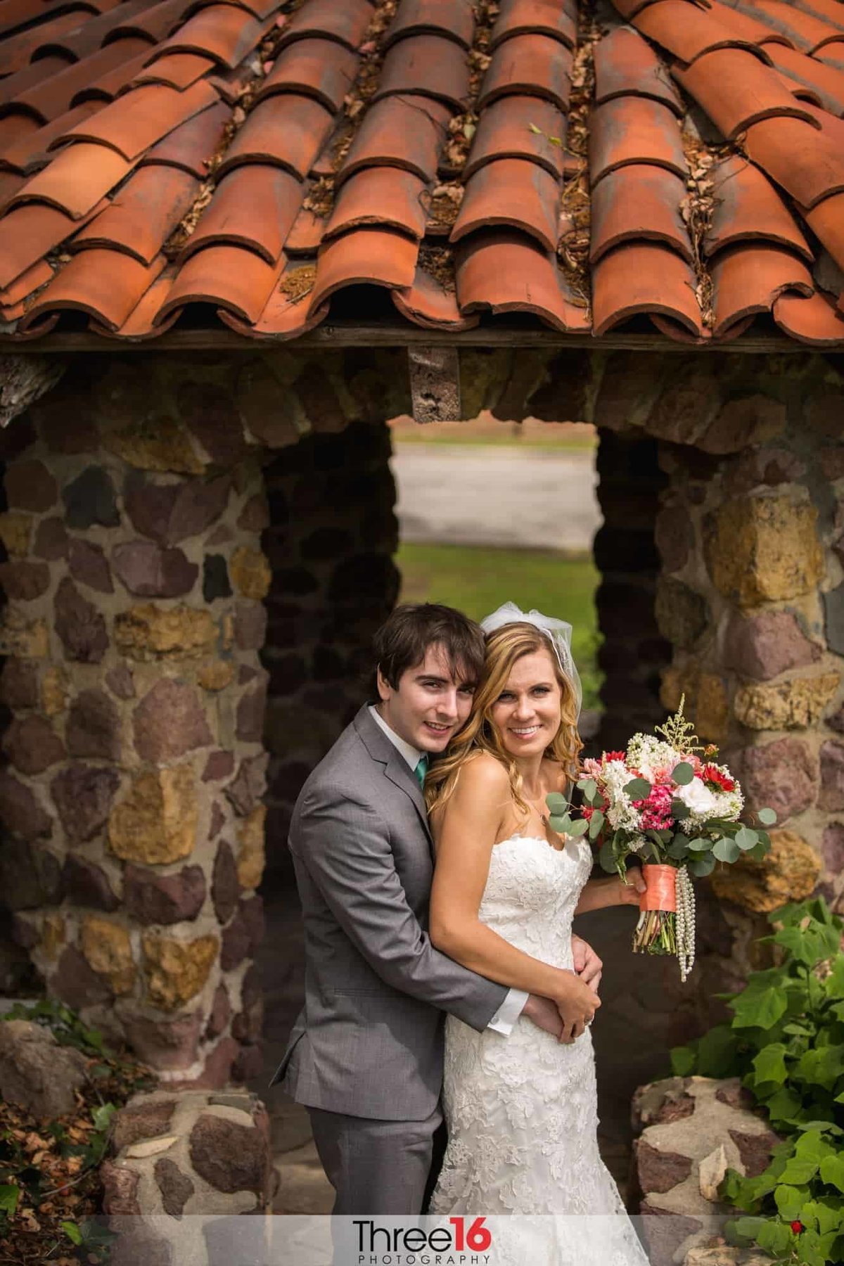 Groom embraces his Bride for photos in front of cobblestone gazebo
