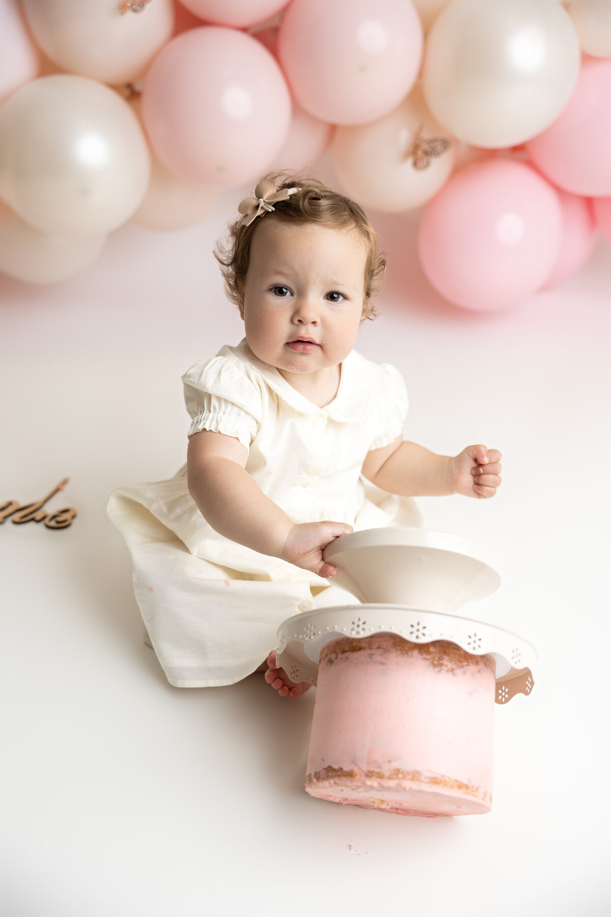 Baby girl cake smash with pink and white balloons, butterflies, and pink cake