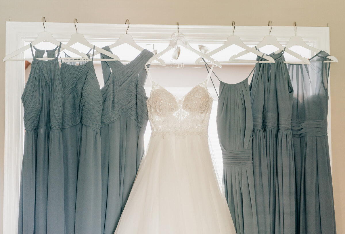 Bride's wedding dress hung beside light blue bridesmaids dresses before the wedding