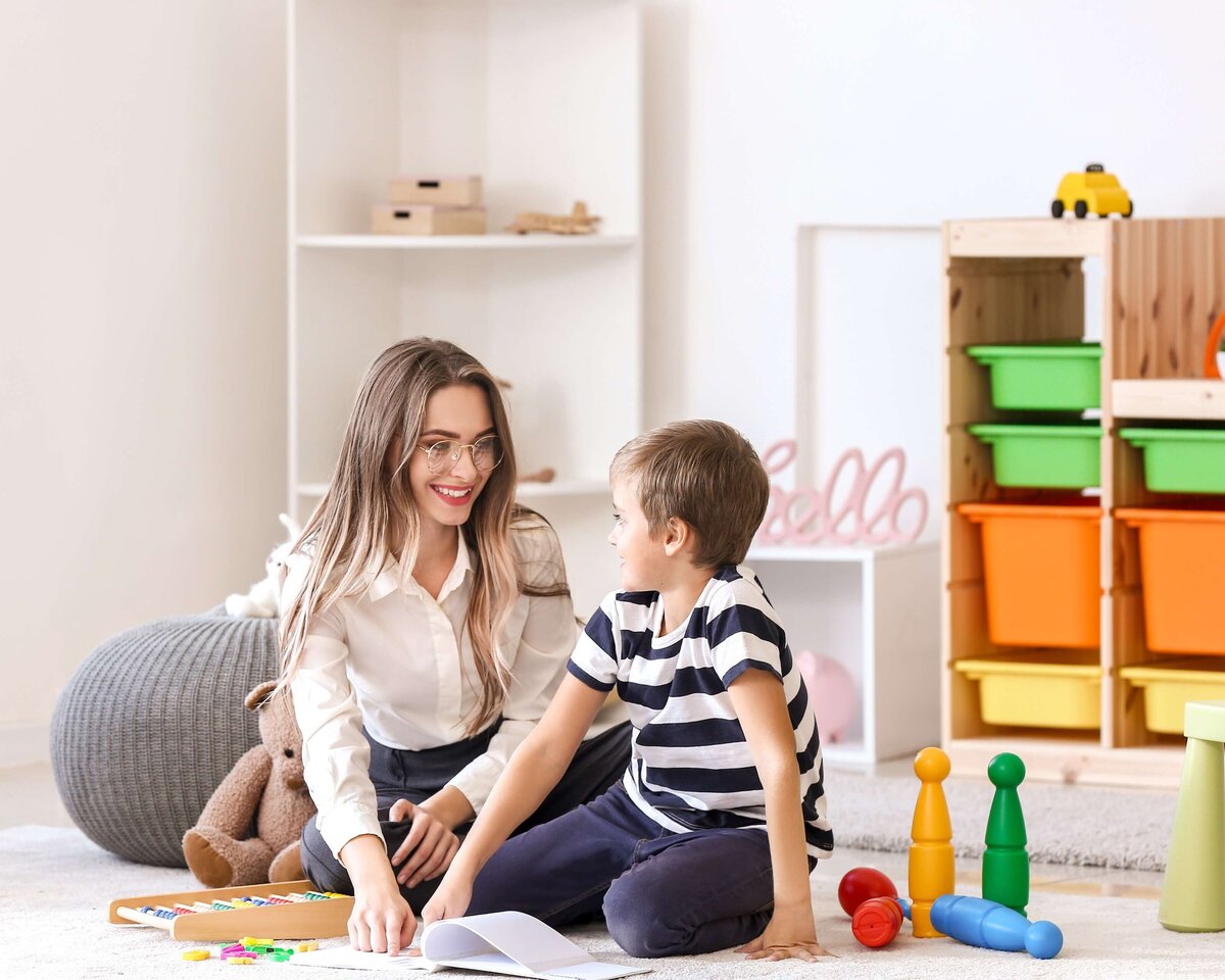 A speech language pathologist sitting with a school aged boy in speech and feeding therapy working on articulation exercises