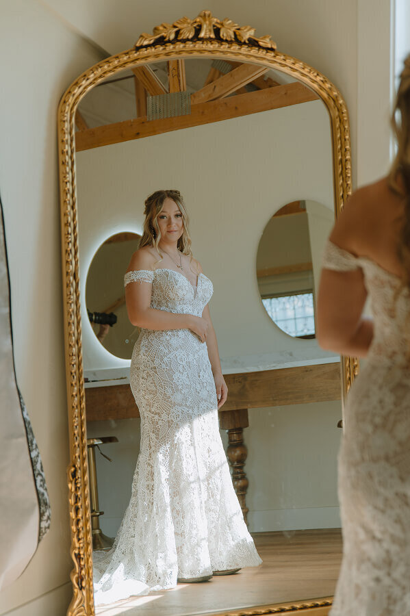 A woman looks at herself in the mirror on her elopement day. She's wearing her wedding dress.