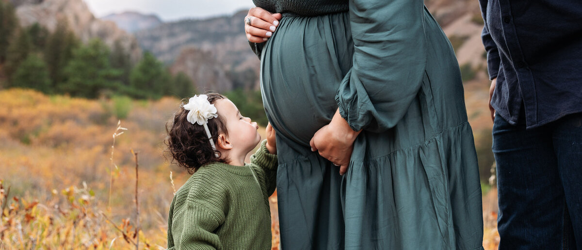 Maternity photo of little girl kissing mom's pregnant belly.