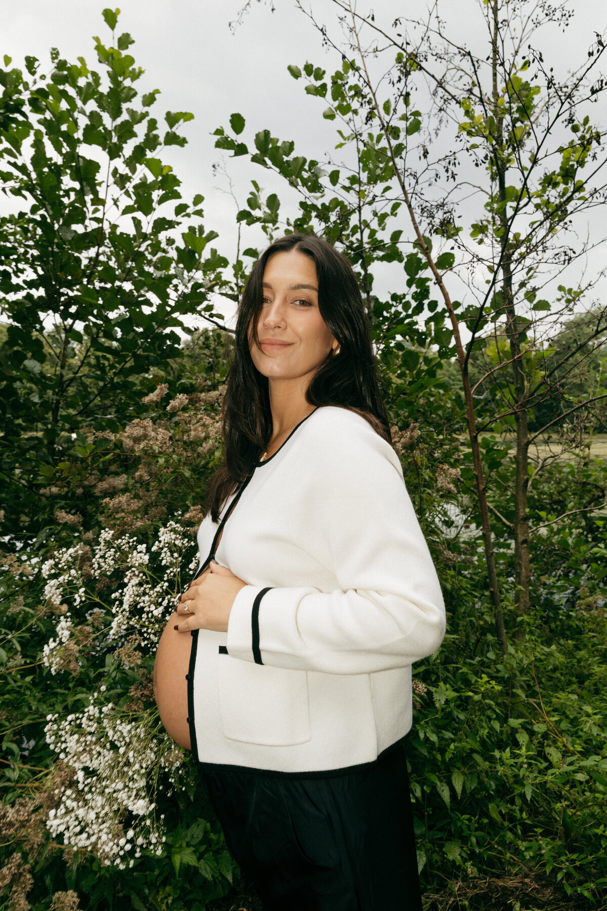 Zwangere vrouw poseert en houdt buik vast met een hand en bloemen in de andere.
