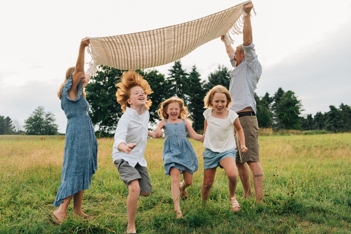 Three kids running under blanket at family session