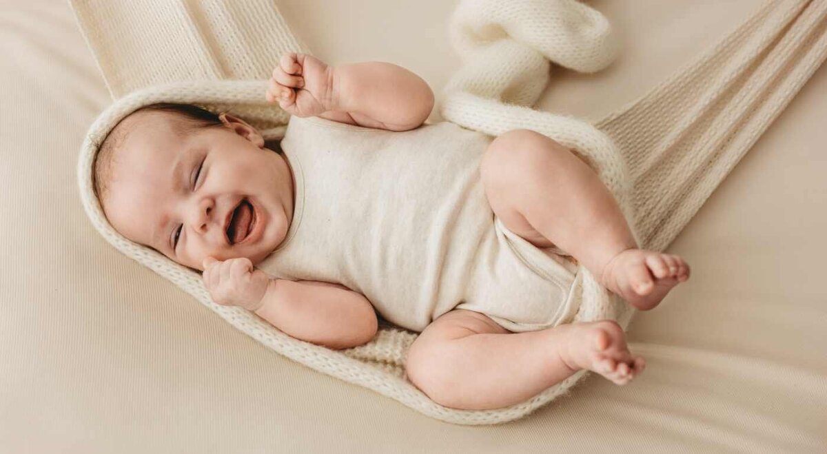 Ruua Hamdan Photography (UK): A baby is wrapped in a white blanket and is laughing.