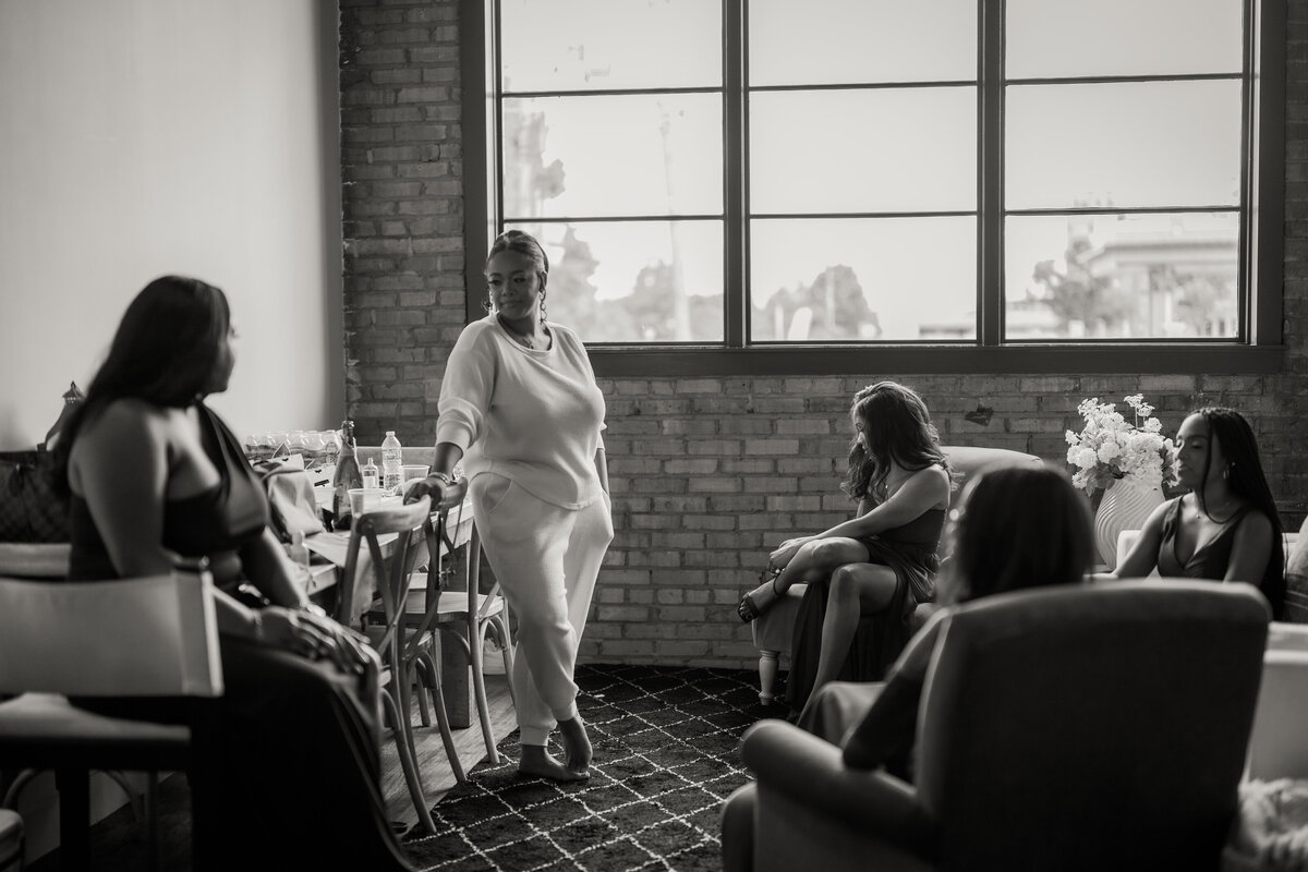 A moody black-and-white shot of the bridal party with the bride illuminated by natural window light at the Dallas venue.