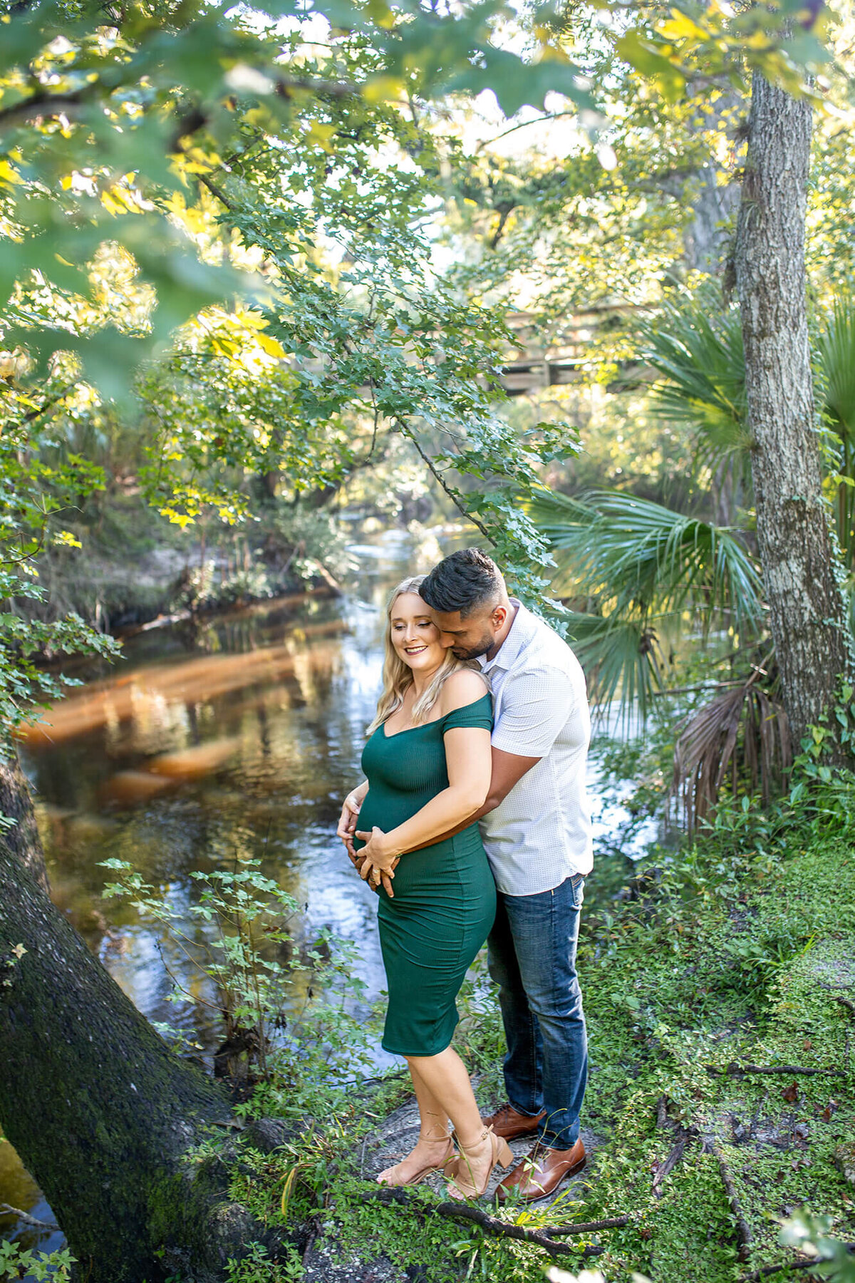 Husband with arms wrapped around pregnant wife standing by the river 