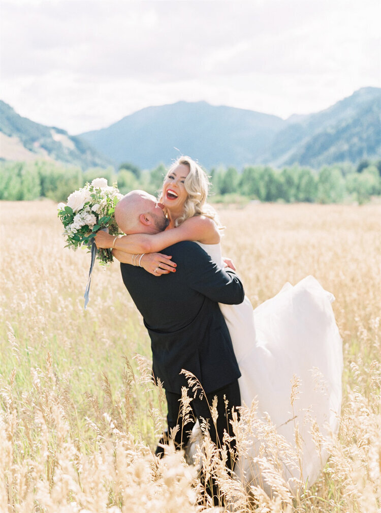 Laughing bride being picked up by the groom in front of a mountain backdrop