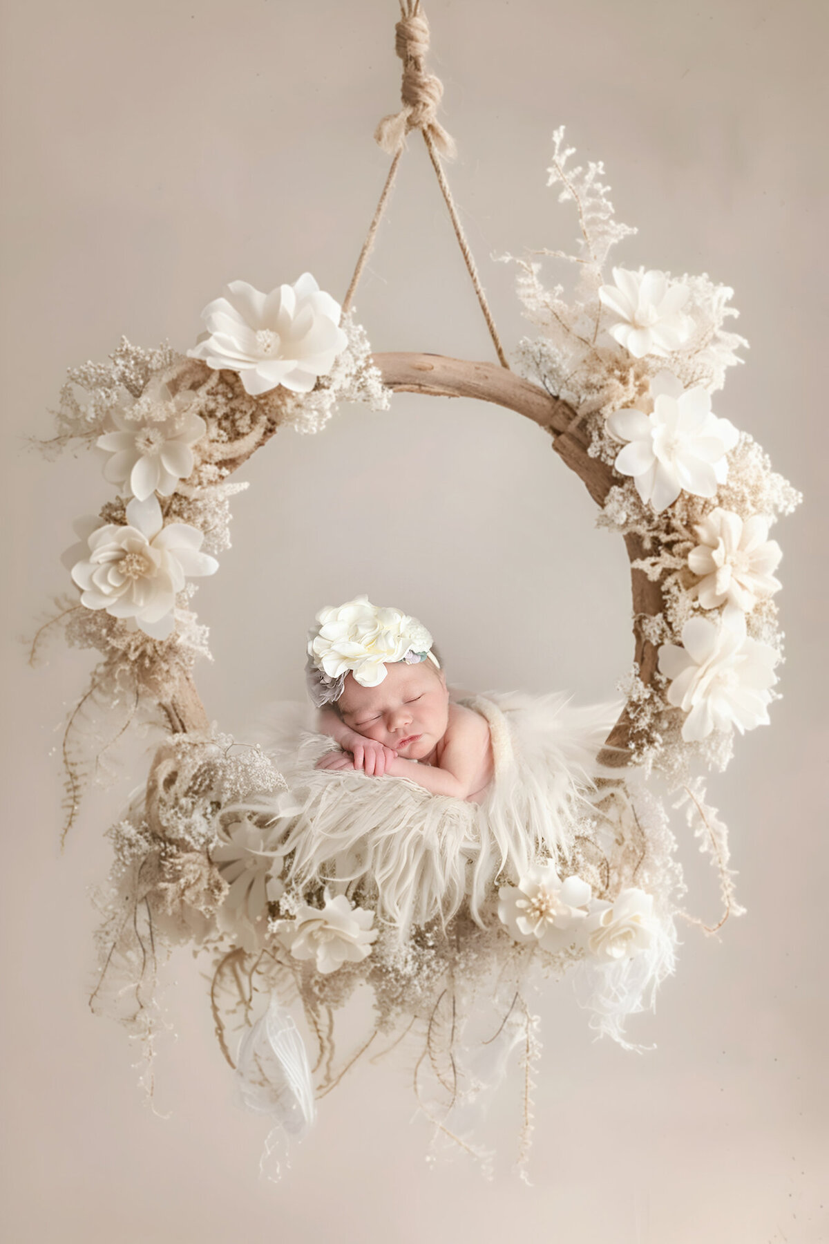 A newborn baby lays on a beige swing covered in flowers for her Des Moines Newborn Photographer