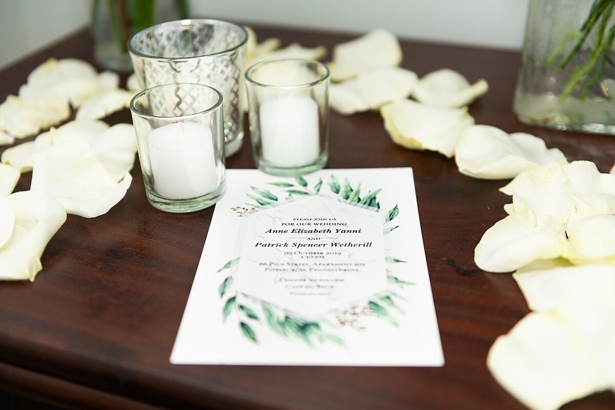 Wedding invitation surrounded by white votives and white rose petals
