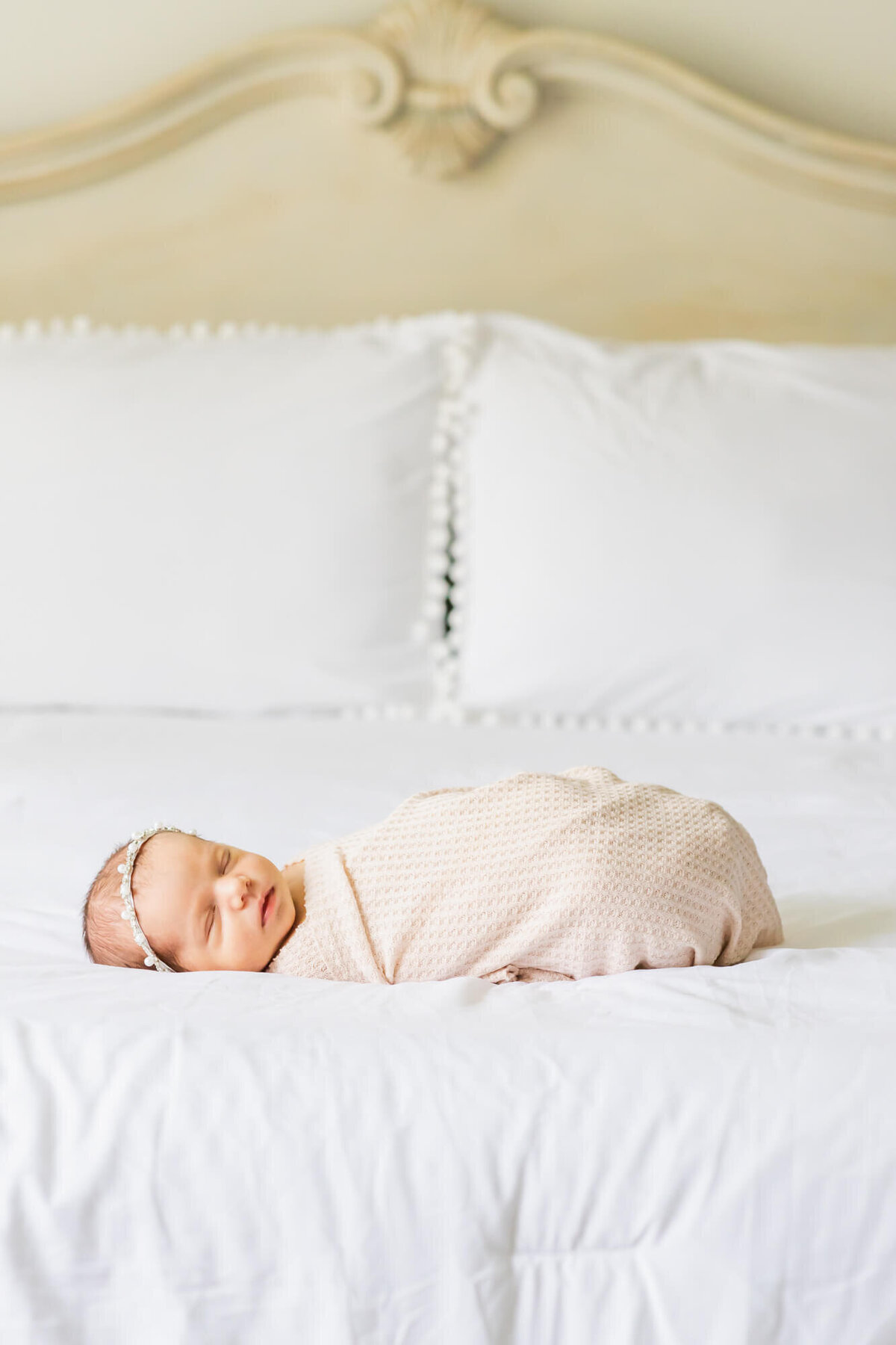 Newborn baby girl laying on a bed with a white boho comforter