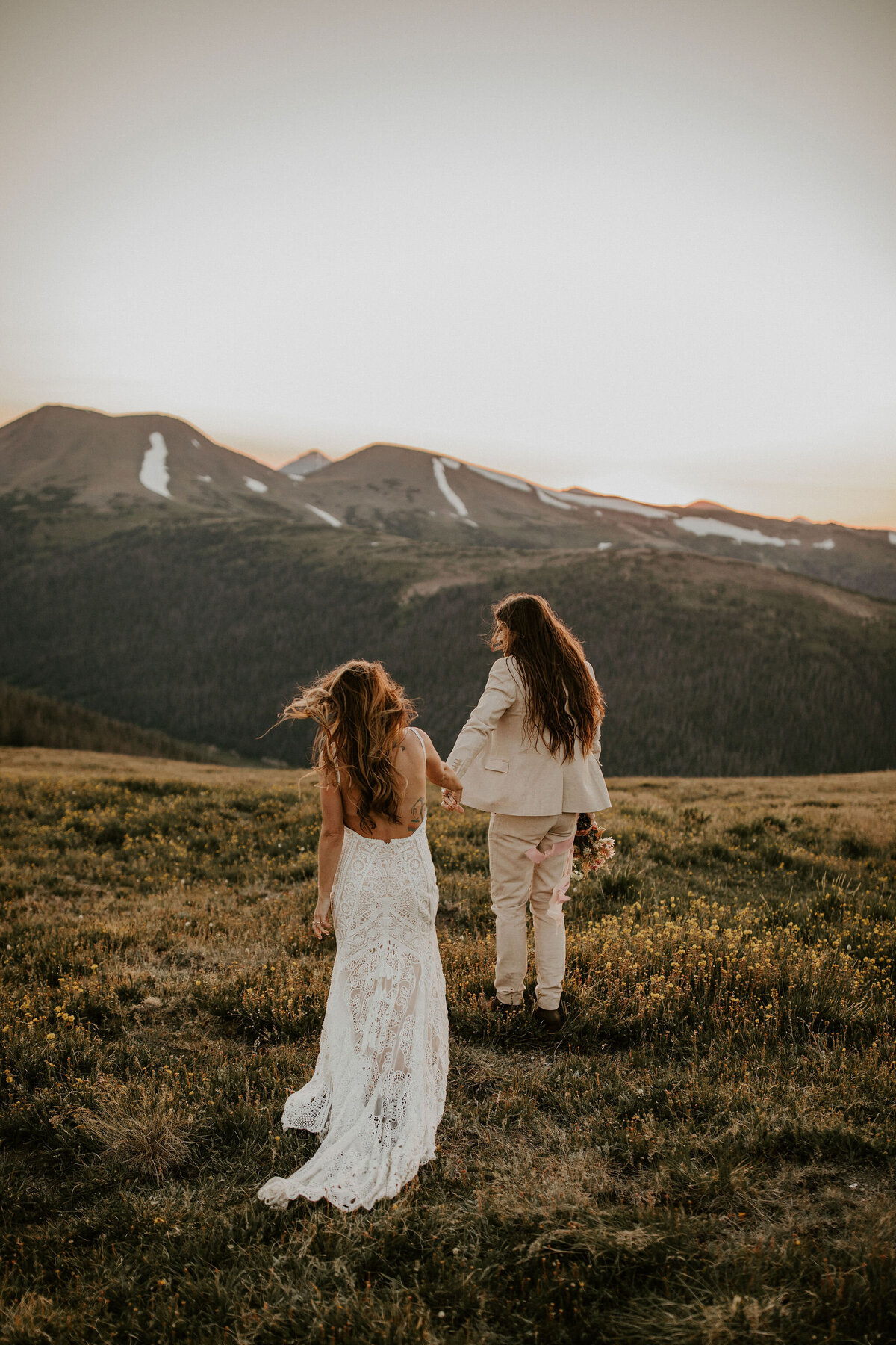 bride and groom wearing a white wedding gown and ivory tuxedo holding hands in the mountains