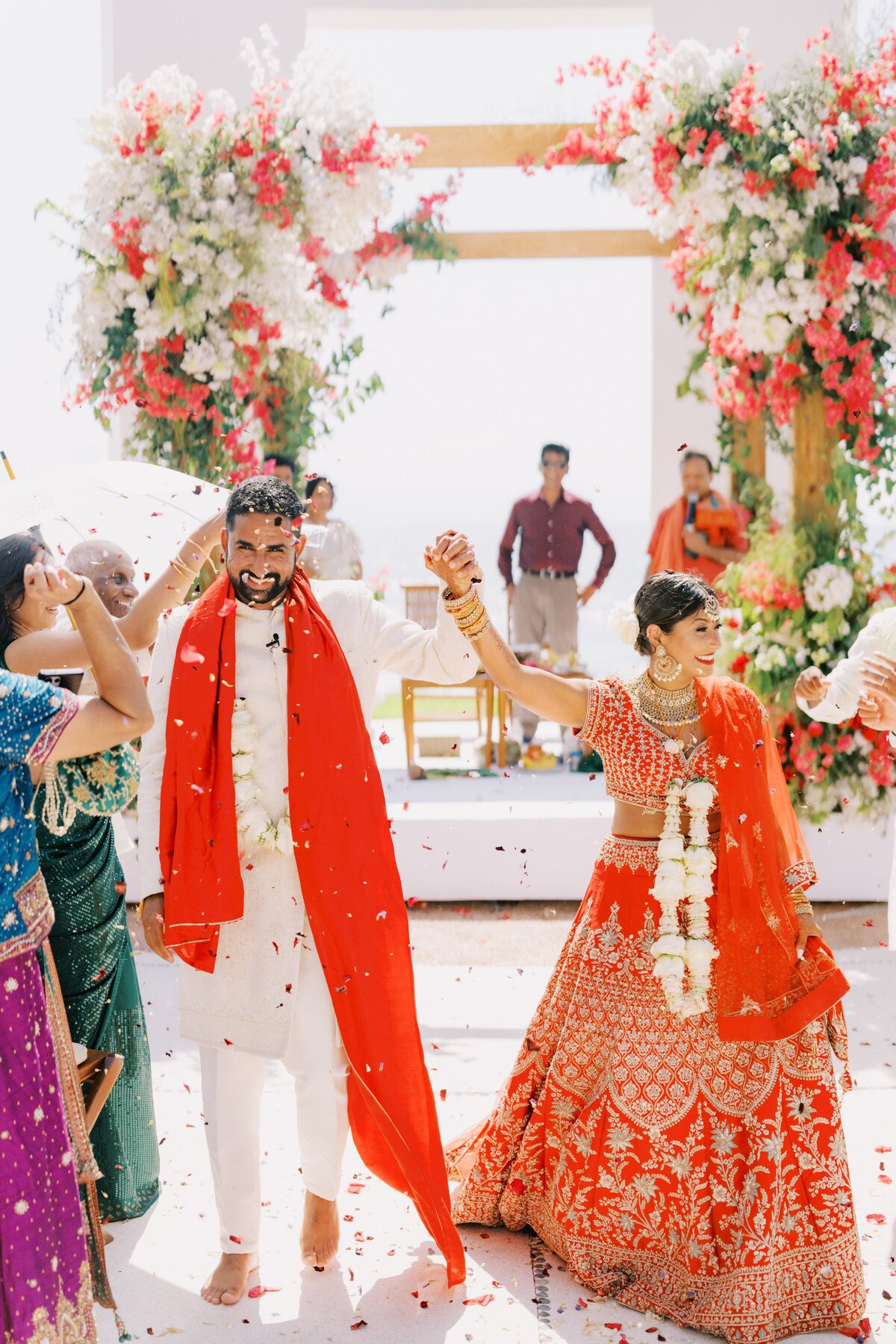 A couple dressed in traditional Indian wedding attire walks hand in hand 