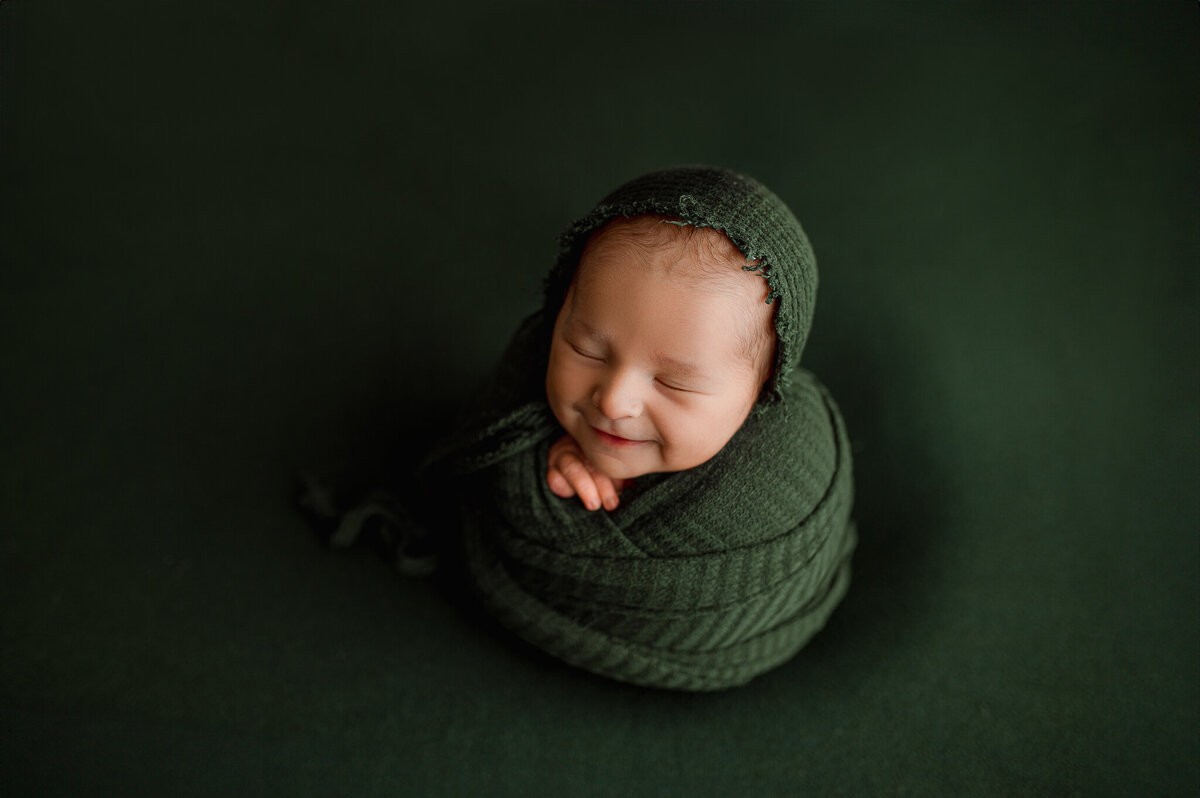 Newborn swaddled in forest green studio
