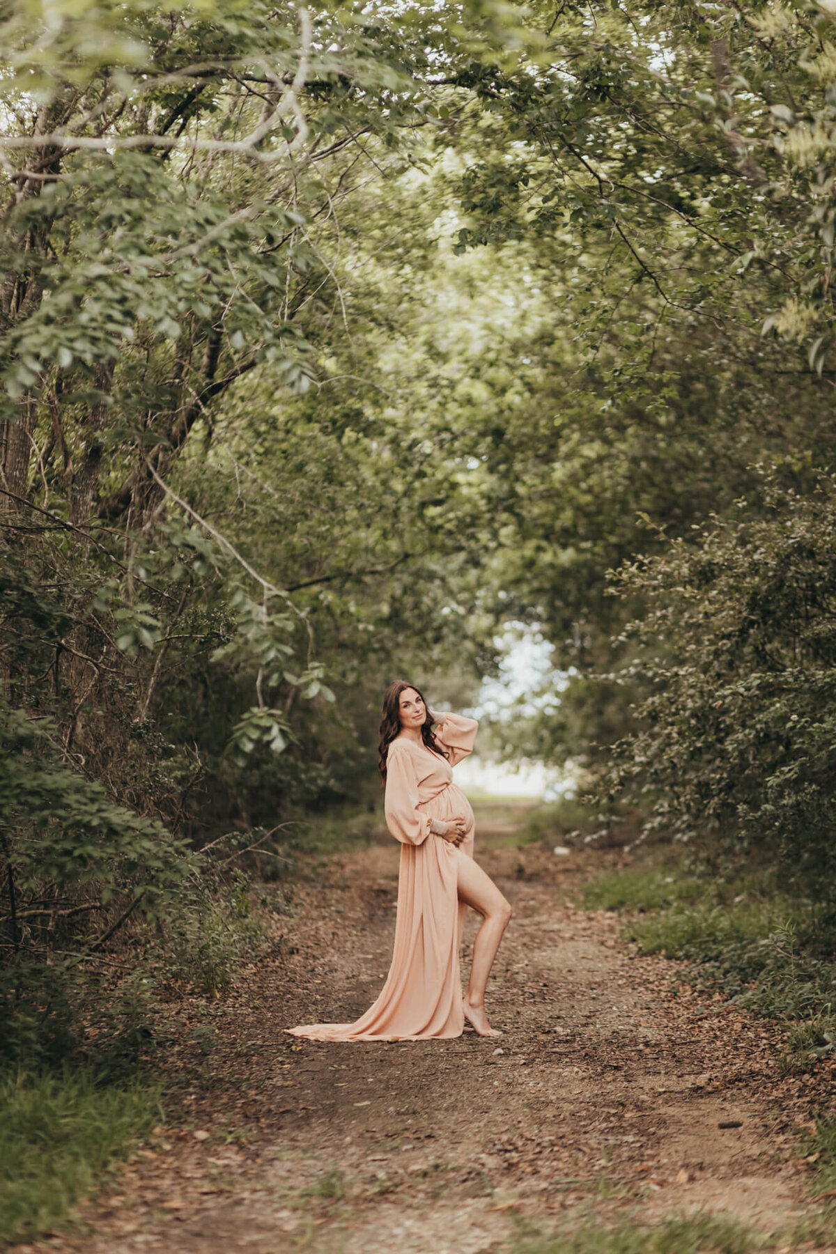 mom pops her knee while holdling belly bump in woods for photo session with ally's photography