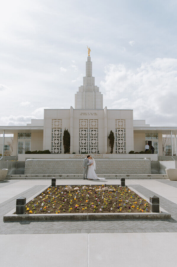 A bride and groom pose for a portrait holding hands in front of an LDS temple near Boise, Idaho.