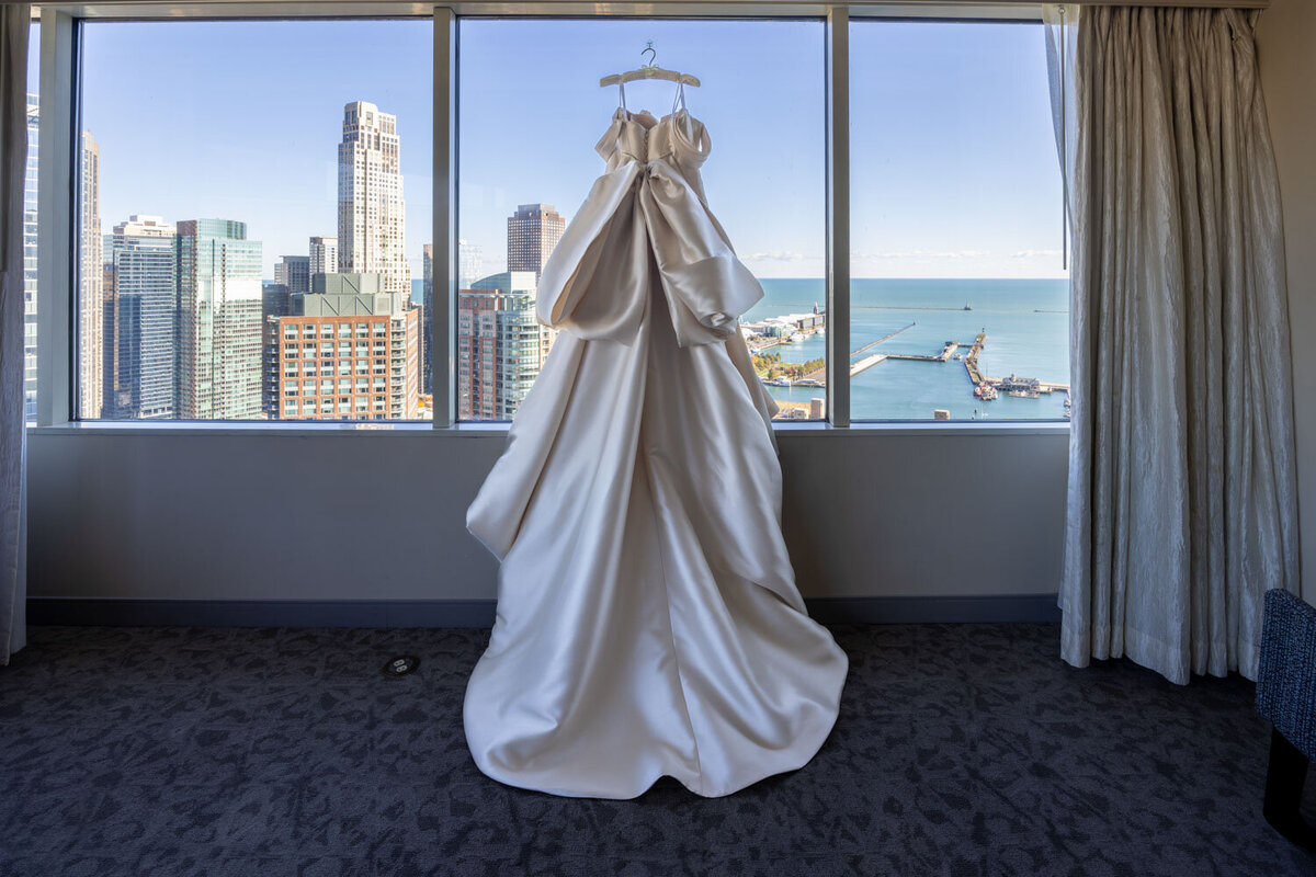 A wedding dress hangs in front of a window overlooking the ocean