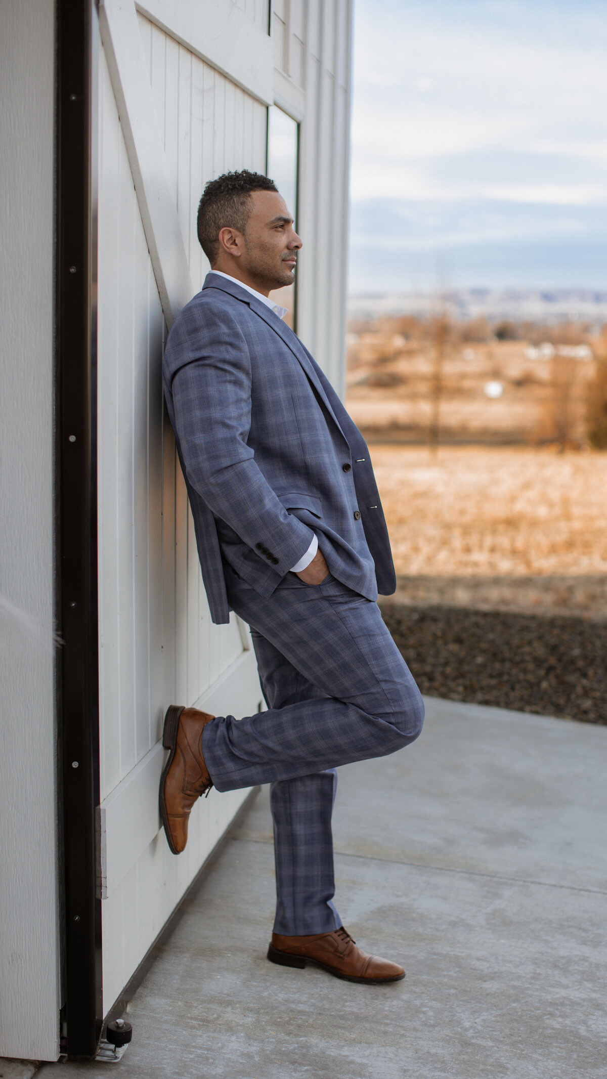 Checkered Suit Brown Shoes vaguely middle eastern man leaning against White Barn