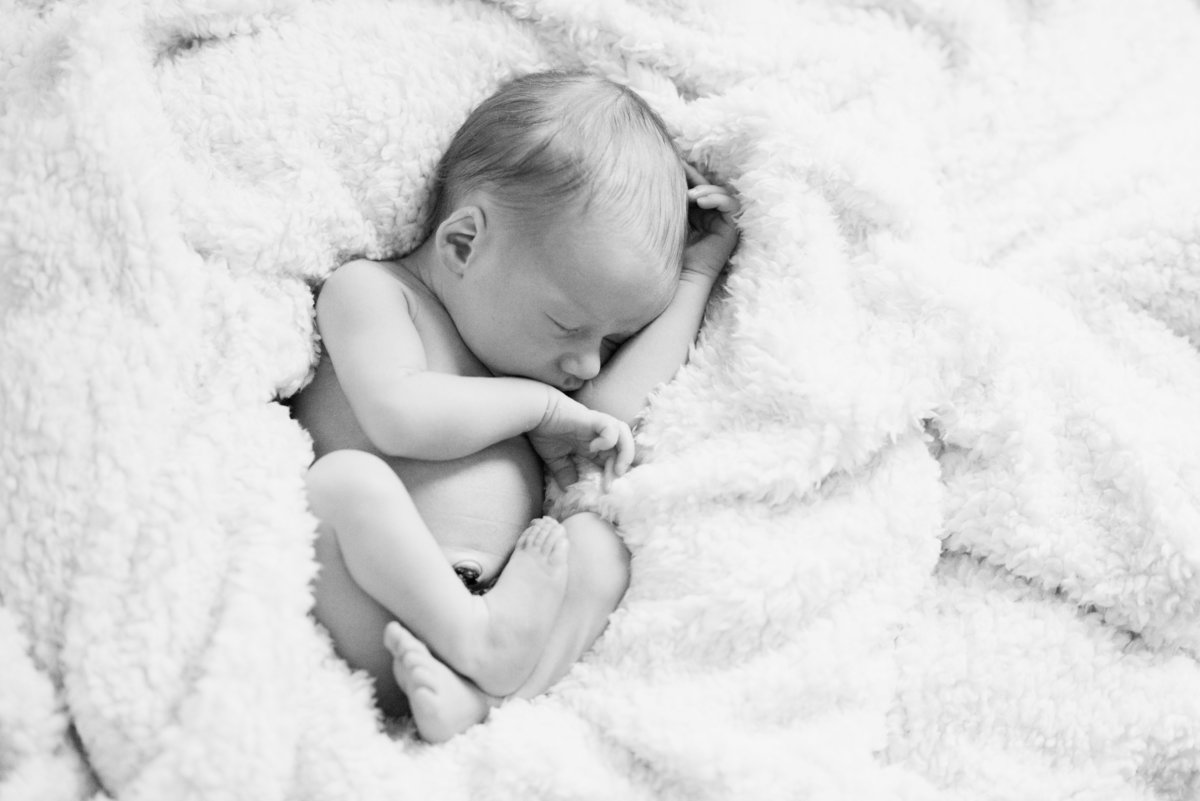 baby curled up in white blanket in black and white photo