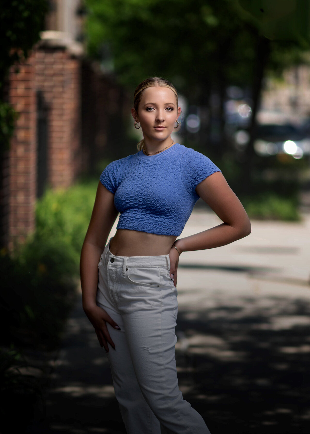 A moment captured by a Pella Senior Photographer of a senior with a hand on her hip in a blue top and white pants