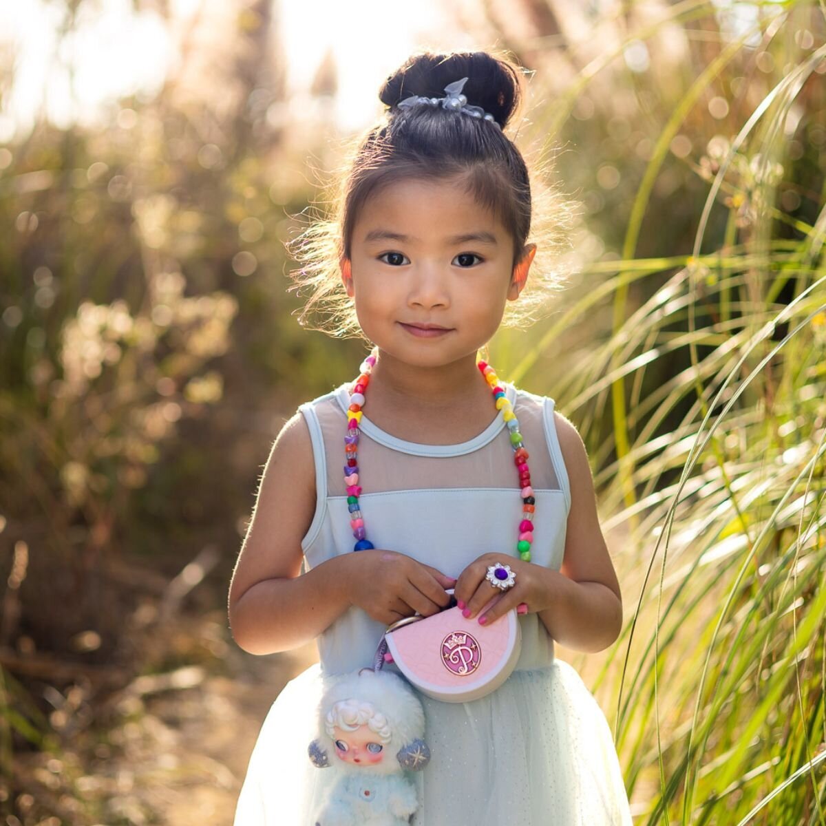 Young girl in soft light wearing a blue dress and colorful beads during Bay Area school photography lifestyle session – Ellobelle Photography