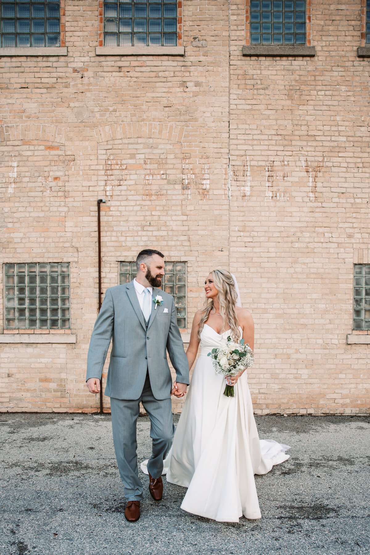 Newlyweds walk while holding hands and smiling each other in an alley with a brick building