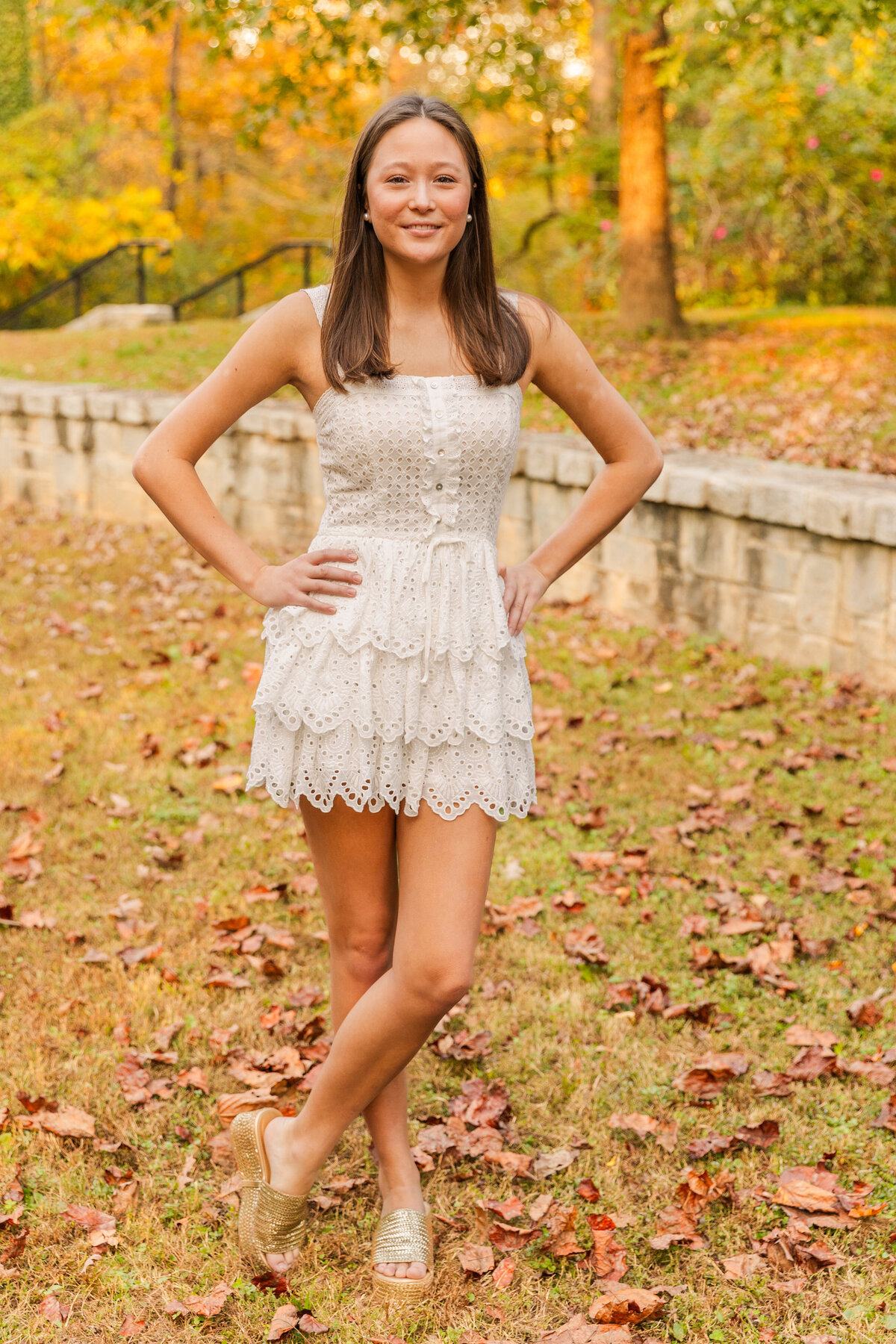 full body shot of teenager gilr wearing a white short dress stnading ankles crosses and hands on hips