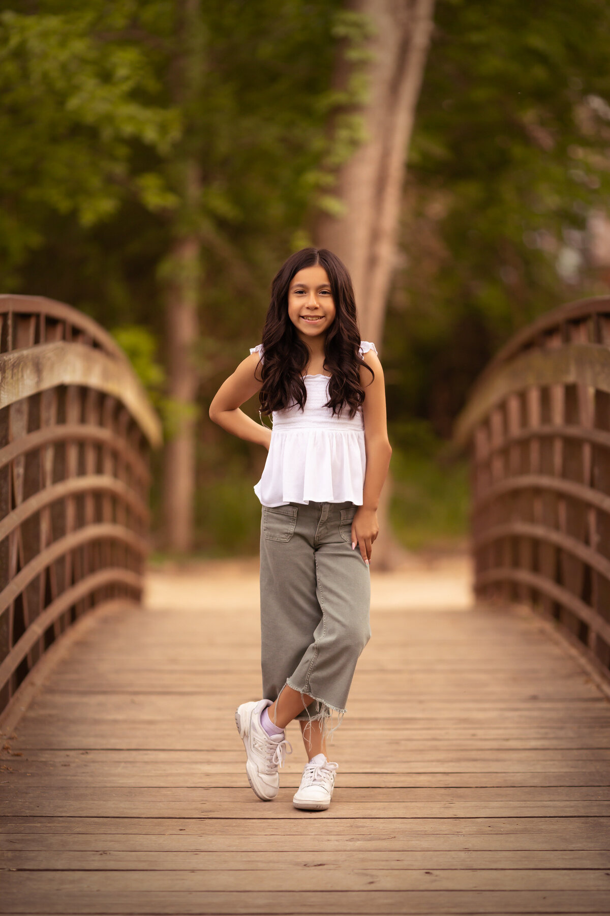 Family portraits in Dallas feature a young girl smiling and posing confidently on a wooden bridge in casual spring attire.