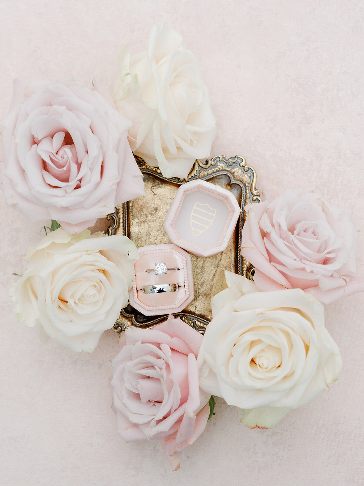 Wedding bands on a golden tray surrounded by white and pink roses.