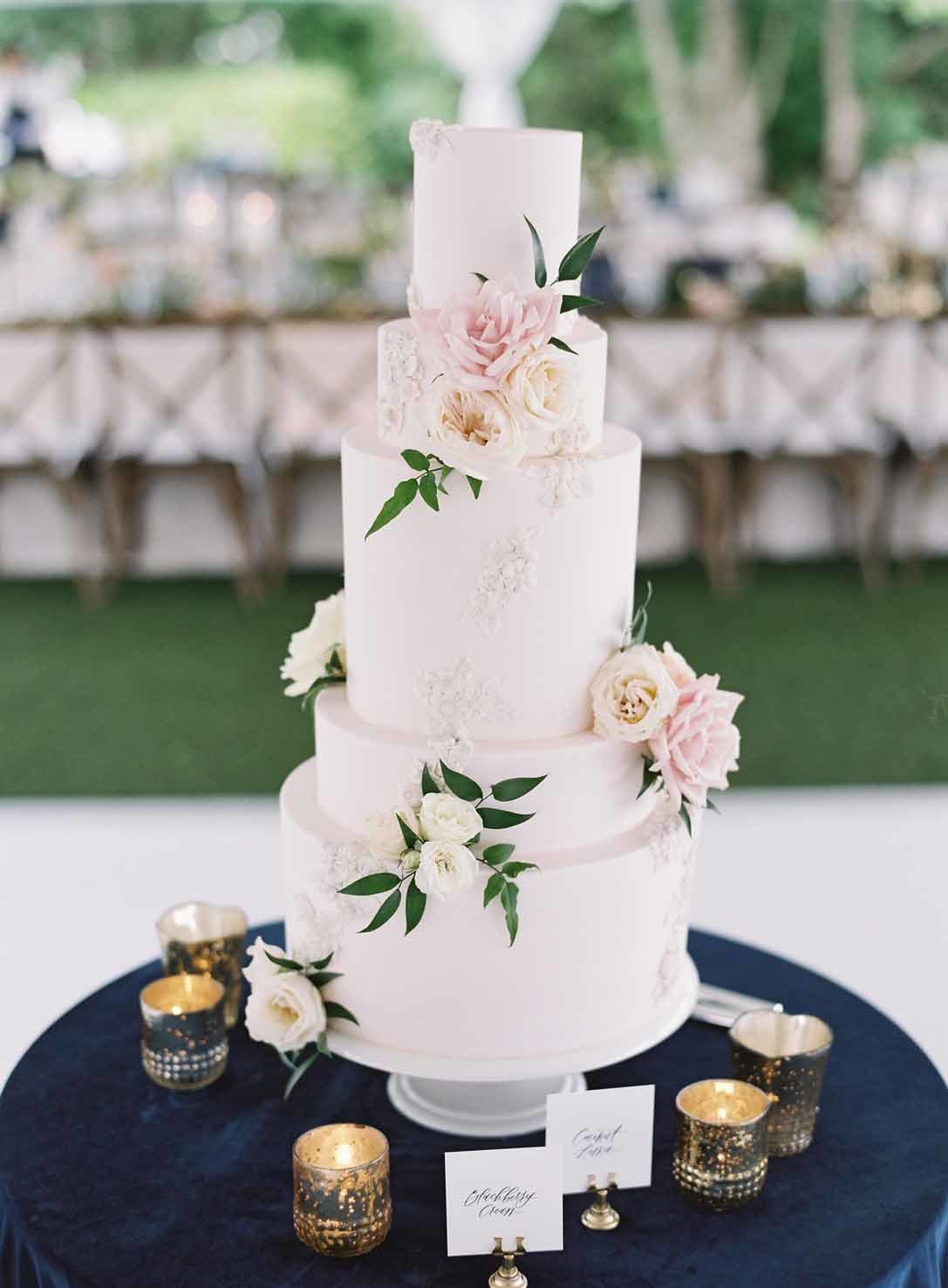 wedding cake with blush and white flowers on table with blue linen and gold votives