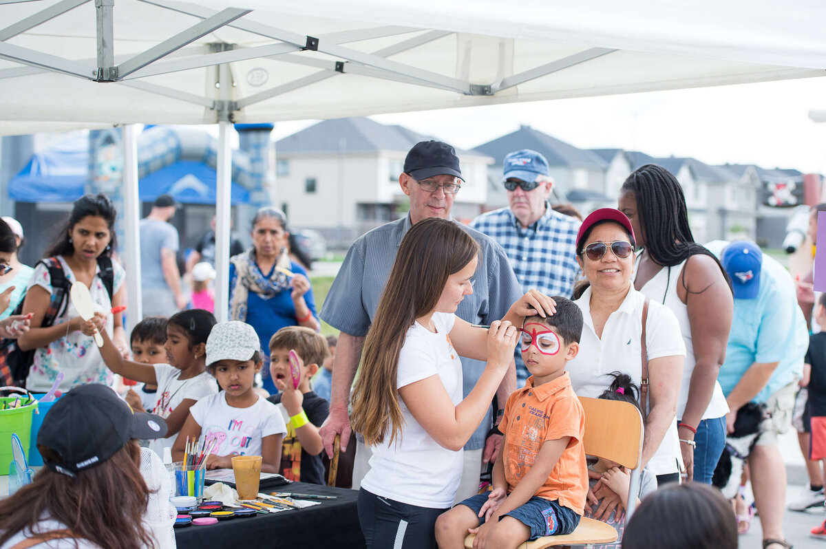 a face painter drawing on a little boy's face as part of a corporate children's event.  Captured by Ottawa Event Photographer JEMMAN Photography COMMERCIAL