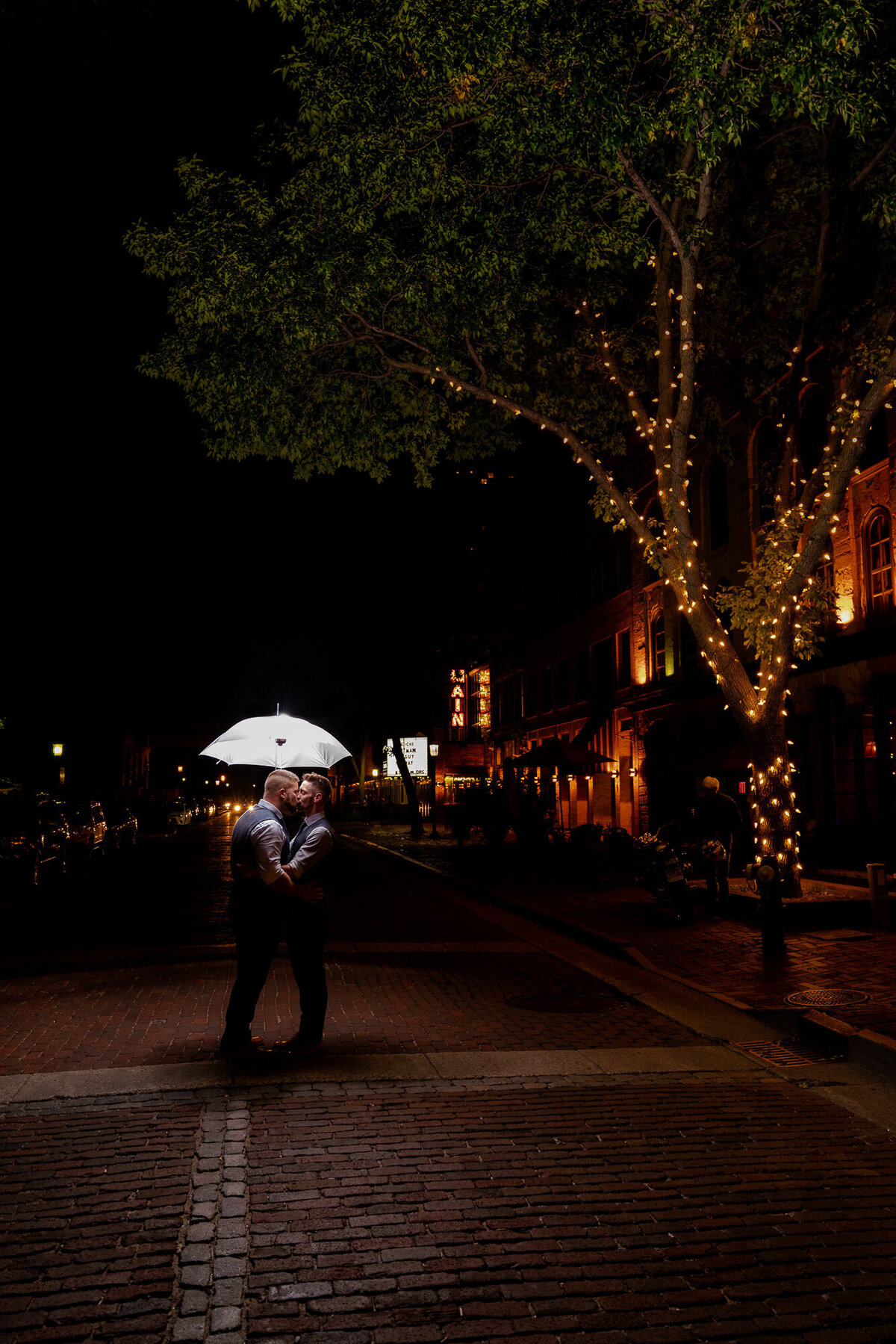 Grooms kiss at night on the cobblestone in Minneapolis, Minnesota.