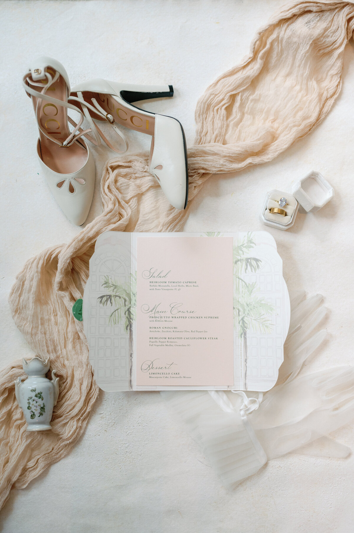 A sophisticated flat lay featuring elegant white shoes, a beautifully designed menu card, and a soft beige scarf. The neutral tones and refined details create a timeless and stylish composition, perfect for upscale event inspiration and luxury fashion aesthetics.