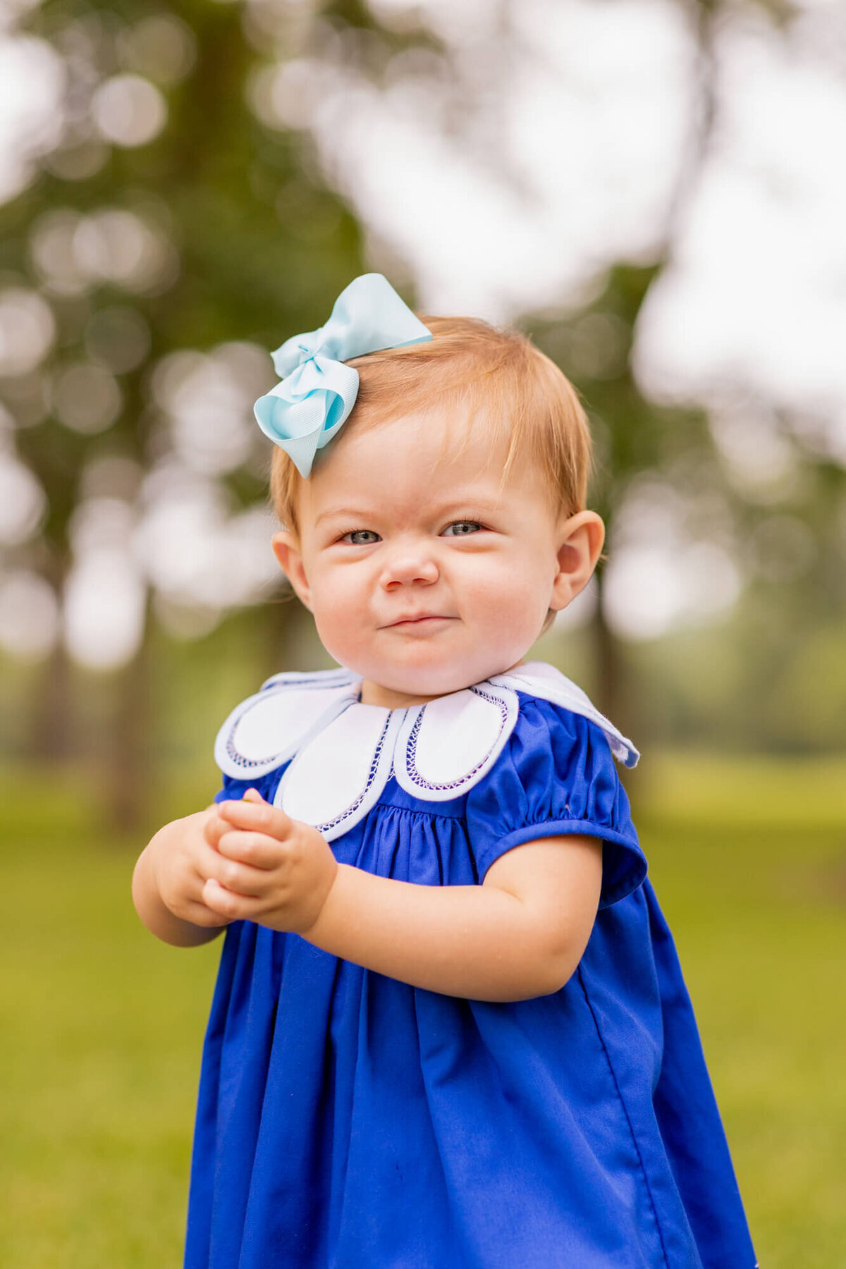 one year old girl in a field in a cobalt blue dress with a scalloped bib