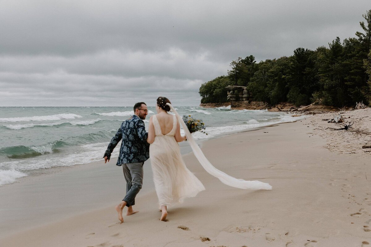 a bride and groom running along the shore on the beach during their elopement