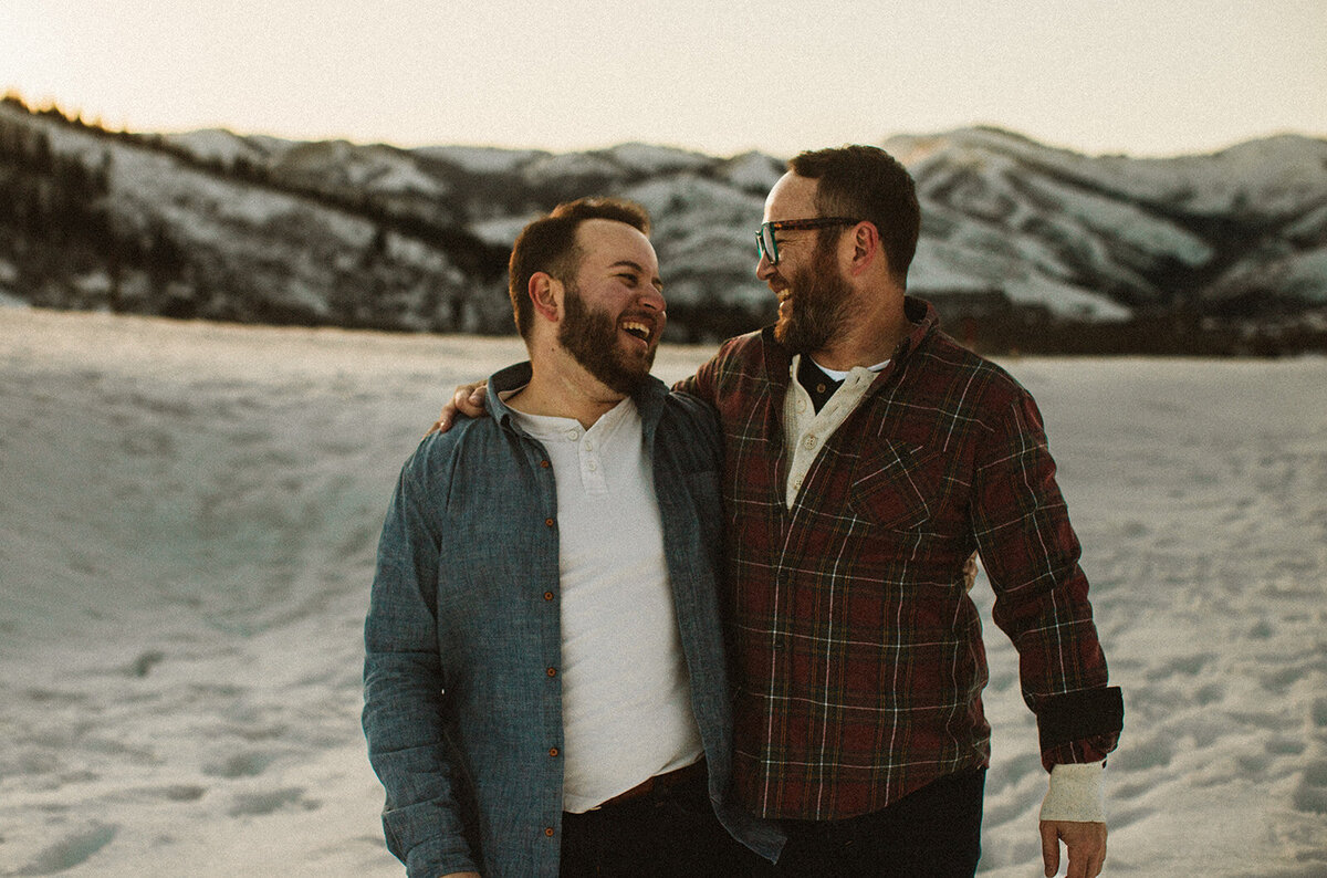 lgbtq two men laughing and smiling at each other in the snow