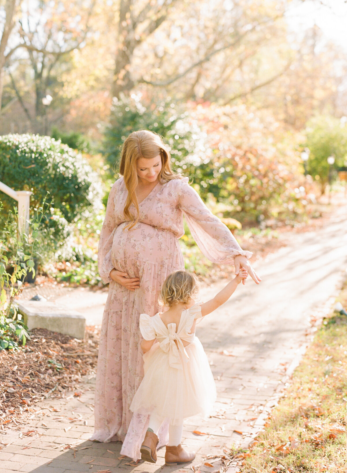 Mom holds daughter's hand and twirls her during a maternity session in Wake Forest NC. Image by Raleigh maternity photographer A.J. Dunlap Photography.