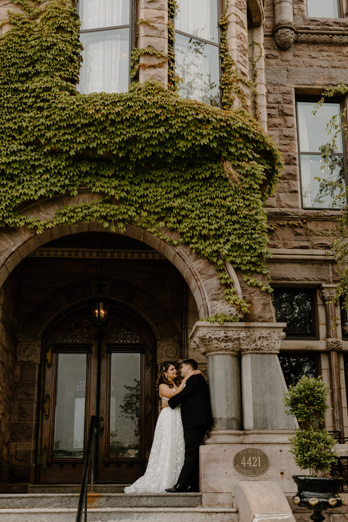 A wedding couple with their arms around each other leaning on an arch 