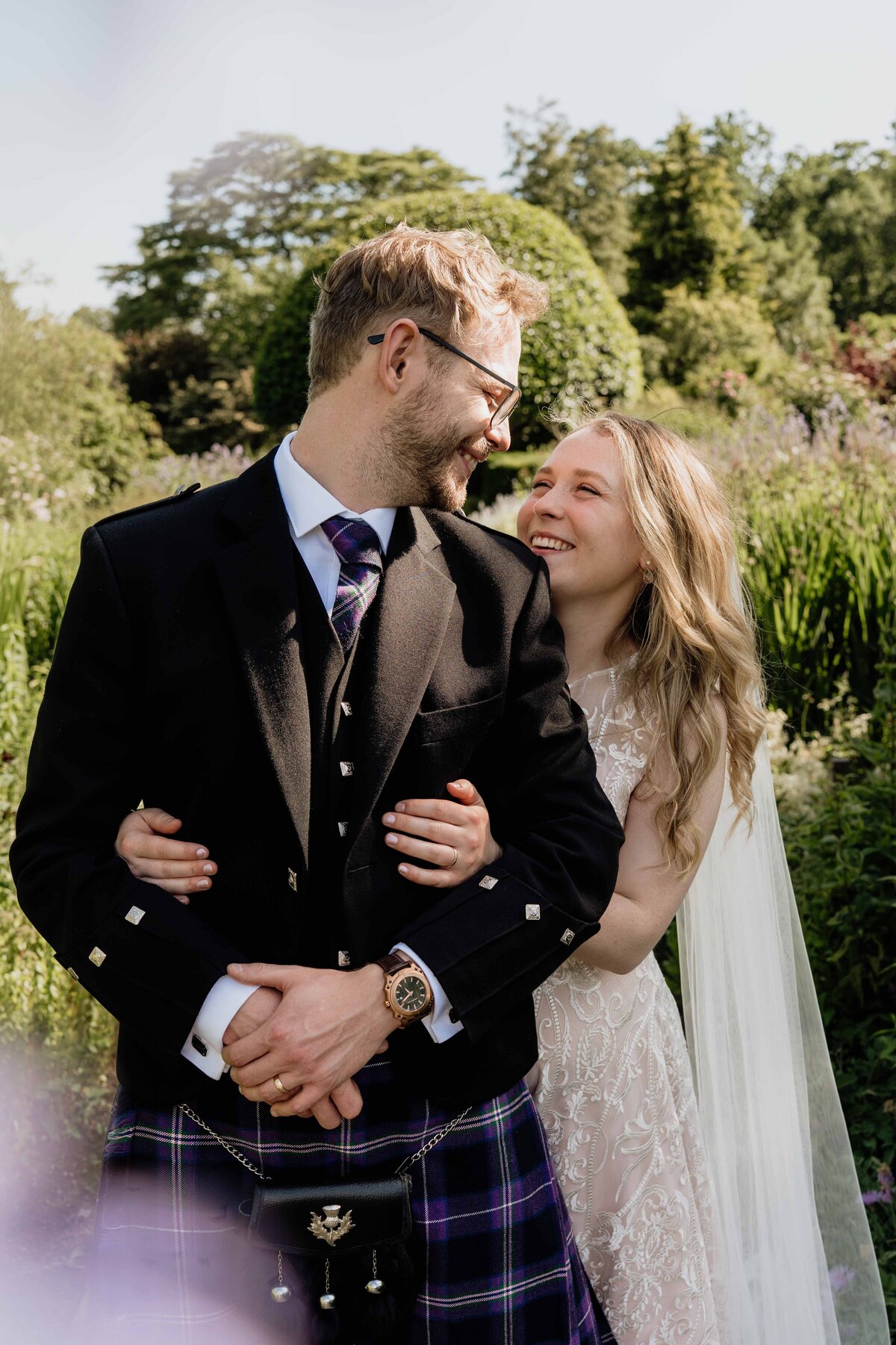 A close photograph of a couple. They wear wedding attire and stand in a walled garden in Crathes Castle in Aberdeenshire.