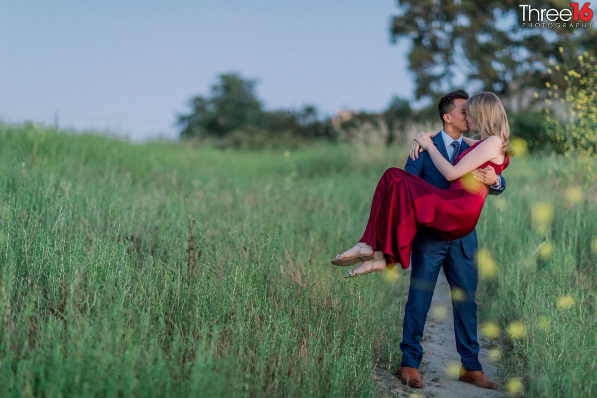 Groom to be carries his Bride in the green grassy area of UC Irvine