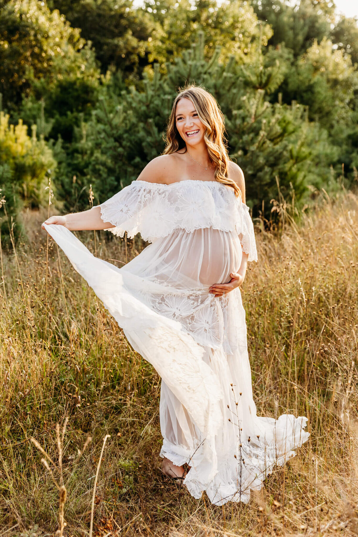 stunning mom in a floral lace dress twirling in front of pine trees during her Green Bay maternity  photo session
