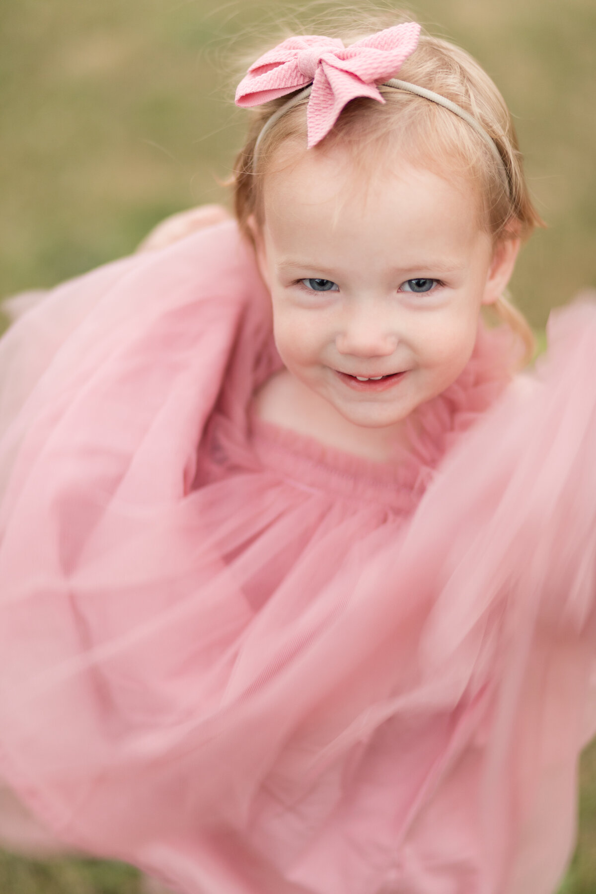 A little girl in a pink dress is smiling at the camera