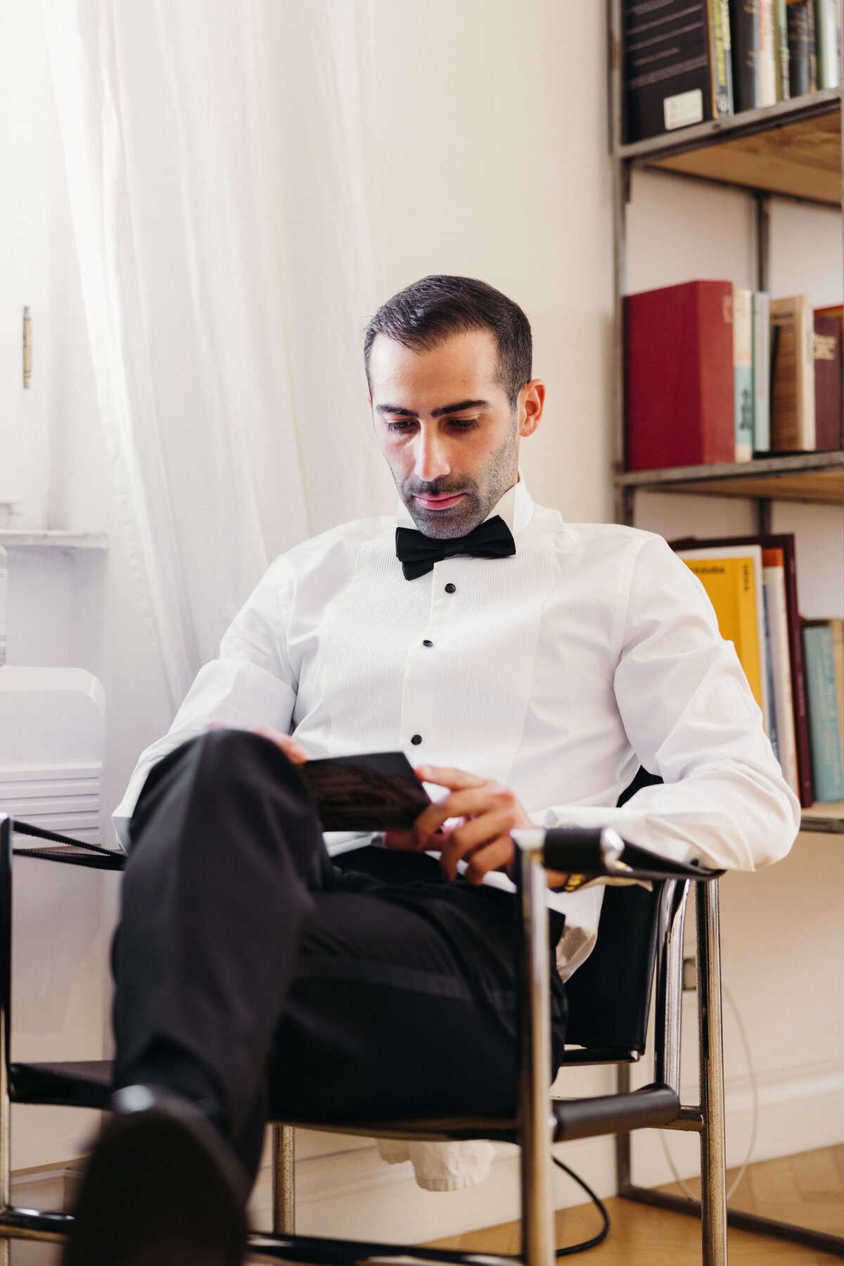 Groom seated and buttoning tuxedo shirt, getting ready in Rome
