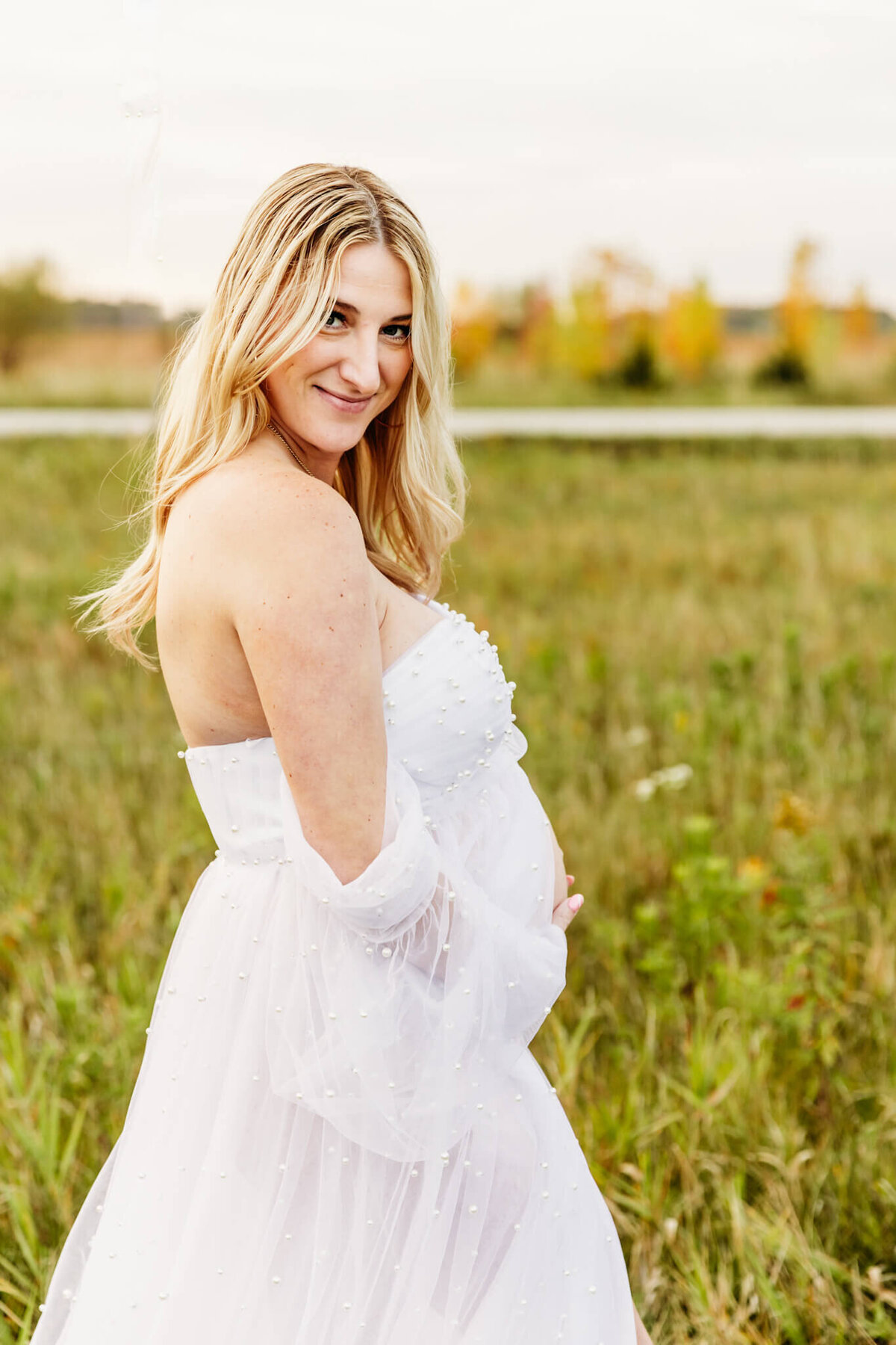 first time mom holding her baby bump and smiling in a beautiful outdoor location near Green Bay wi