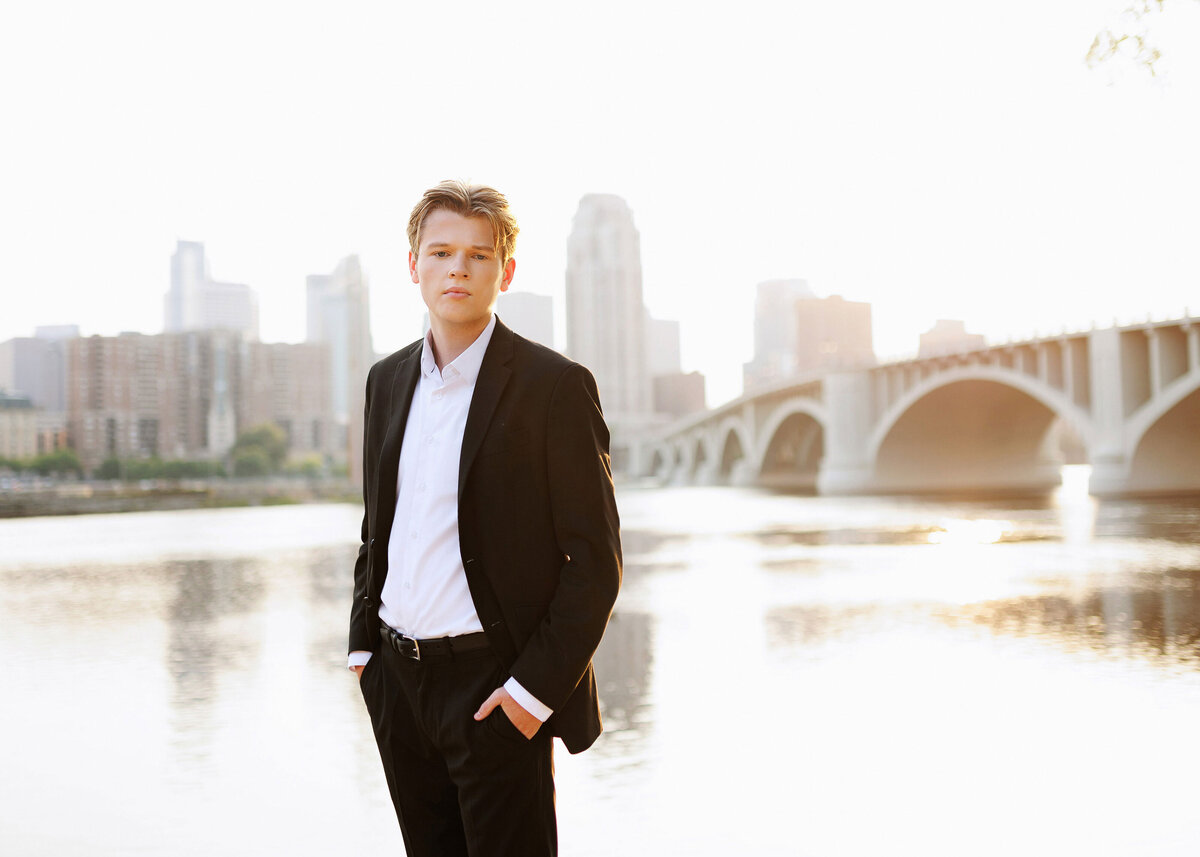 senior guy in formal attire with minneapolis skyline and river bridge in the background