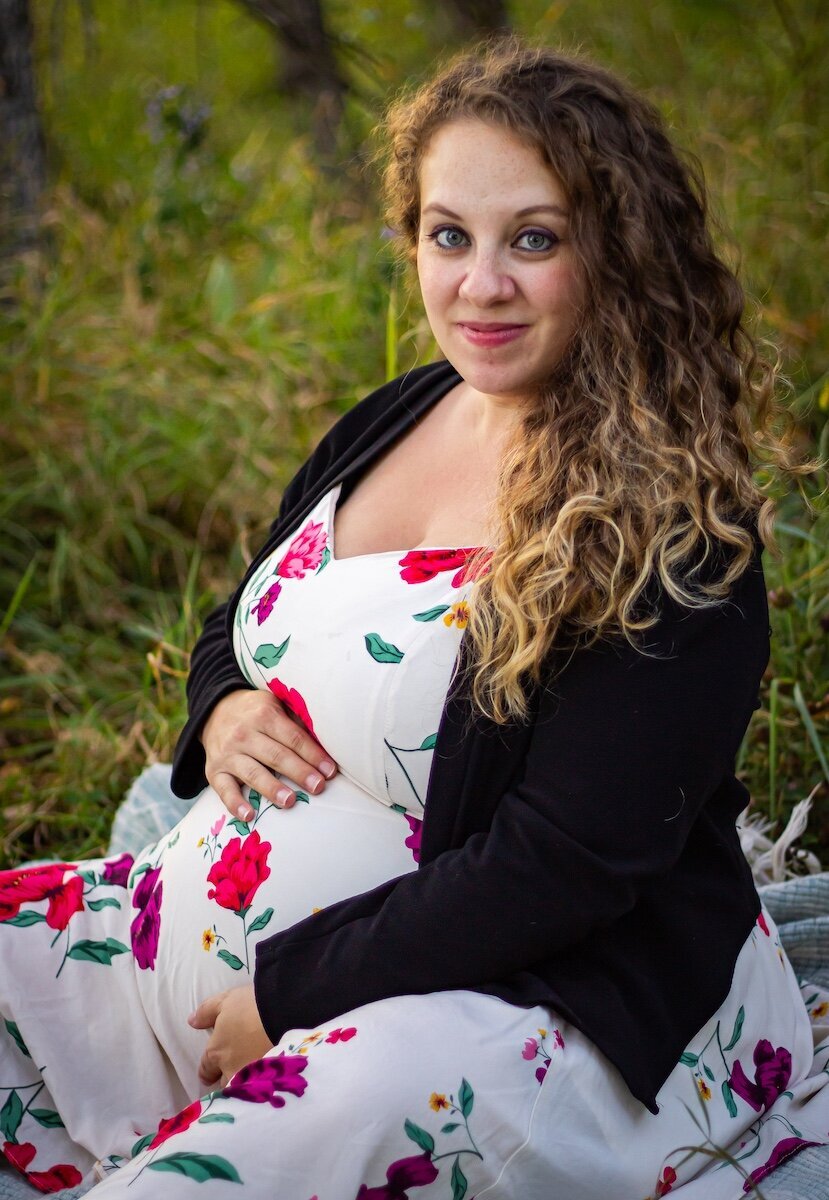 a pregnant woman sits on a picnic blanket holding her belly 