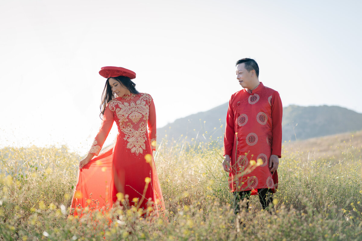 Asian bride and groom couple eloping at Malibu Sate Park wearing Vietnamese red Ao Dai red within golden wildflower field and mountains.